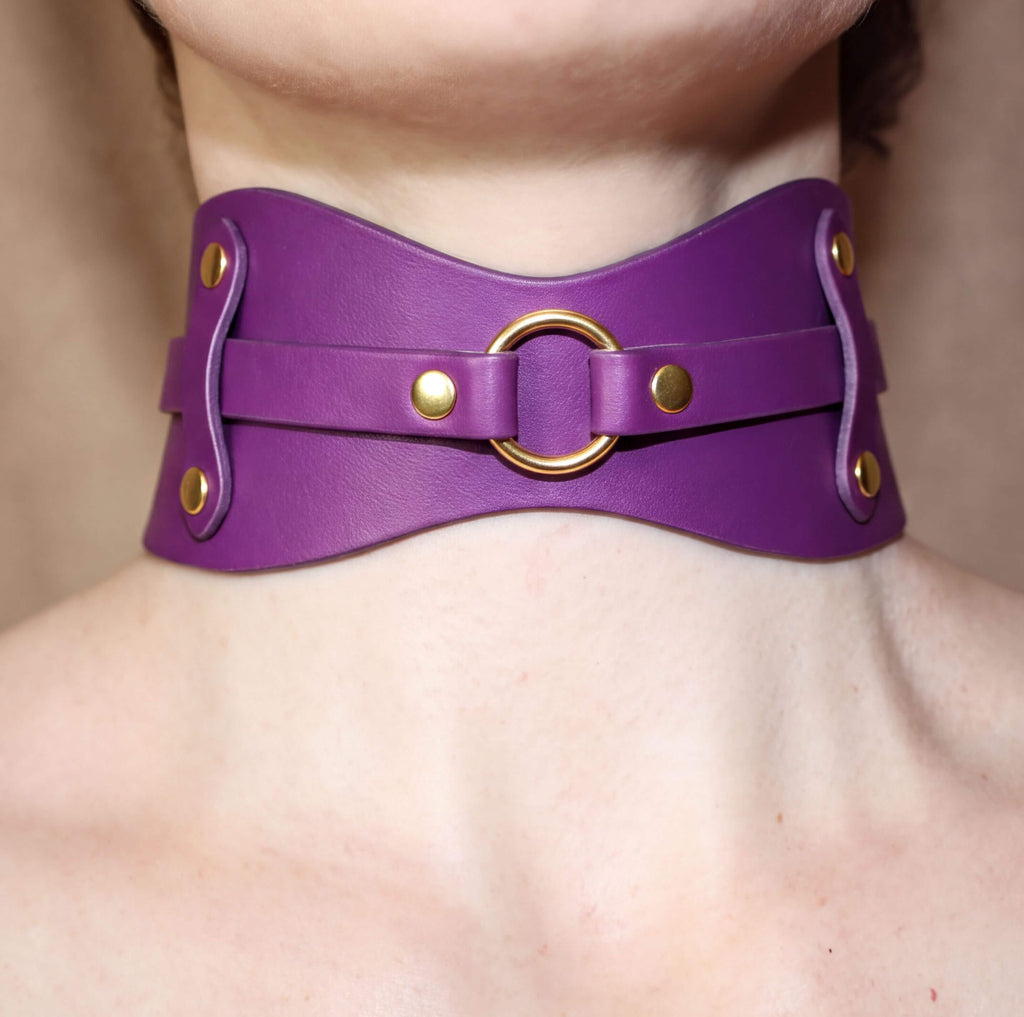 A close-up view of a person's neck and chest area wearing a purple leather choker necklace with a gold ring.