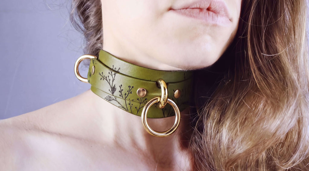 A close-up of a woman's neck and chin wearing a green leather choker necklace with gold rings.