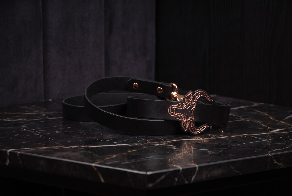 A black leather belt with a gold buckle is placed on a black marble surface.