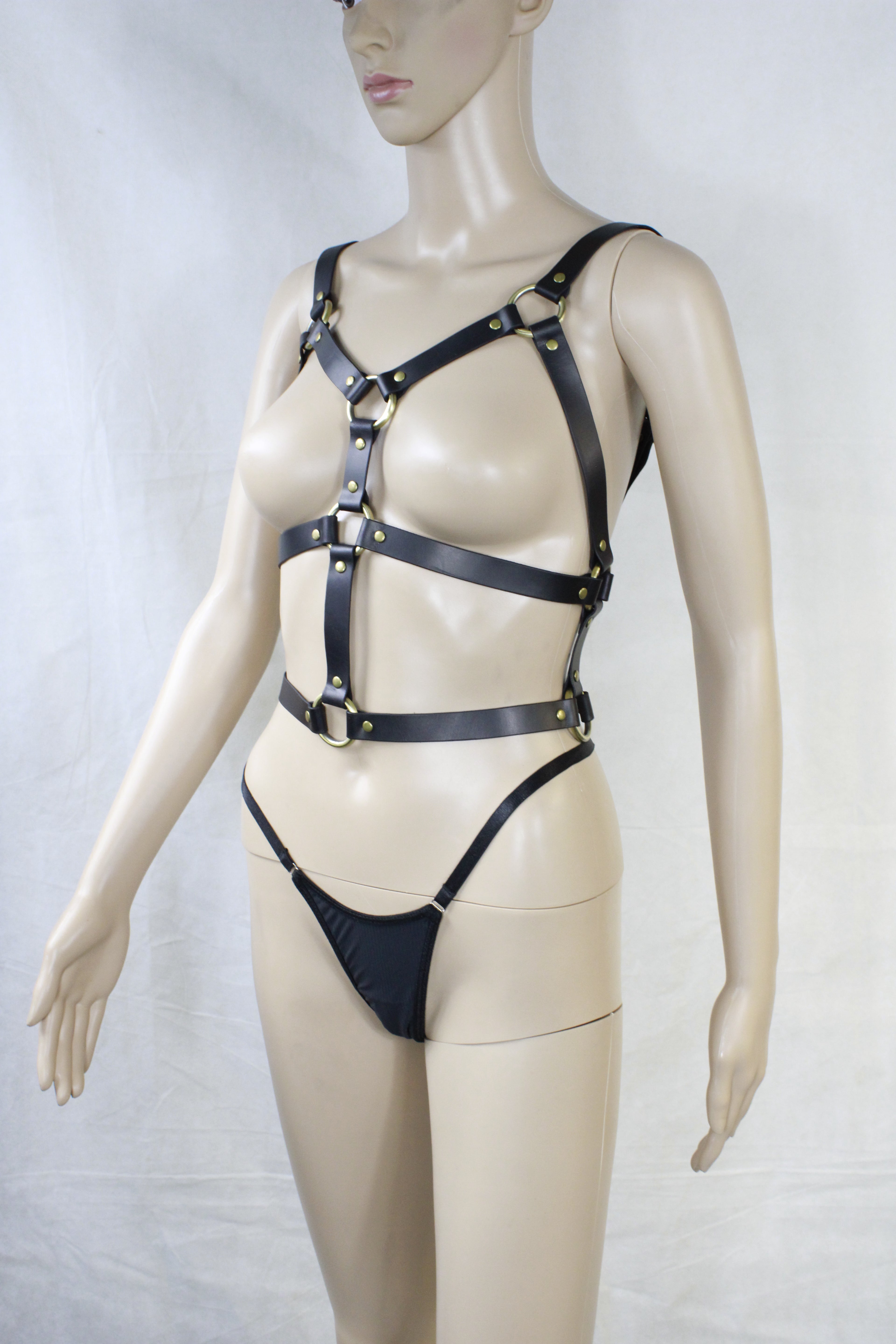 A mannequin wearing a leather harness and straps, with its arms and legs spread out in a relaxed pose.