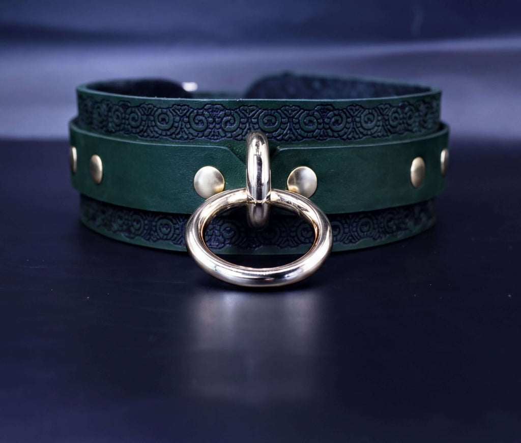 A dark green leather choker necklace with a gold-colored metal ring and a decorative pattern on the band.