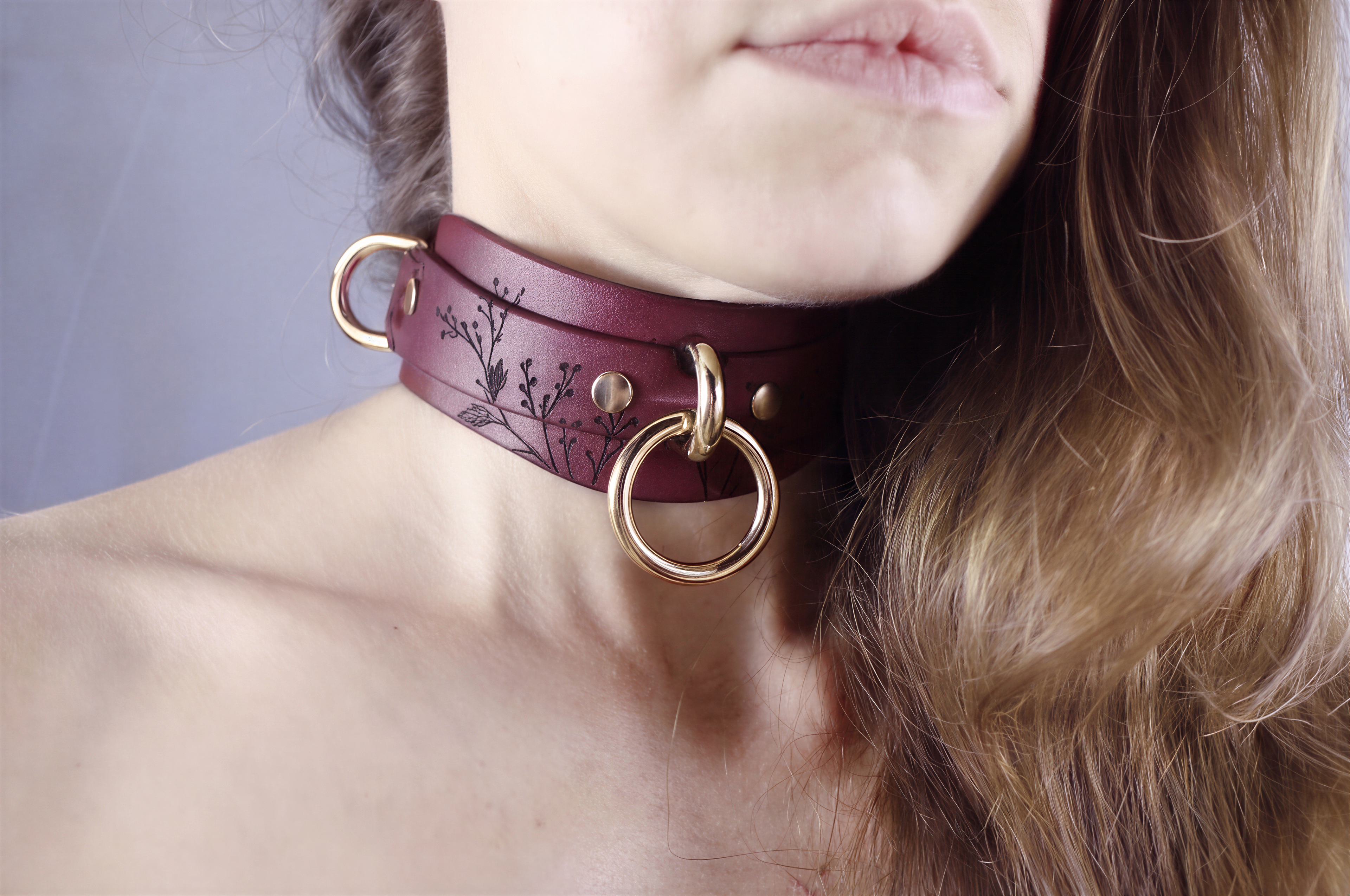 A close-up of a woman's neck and chin wearing a burgundy choker necklace with gold rings.