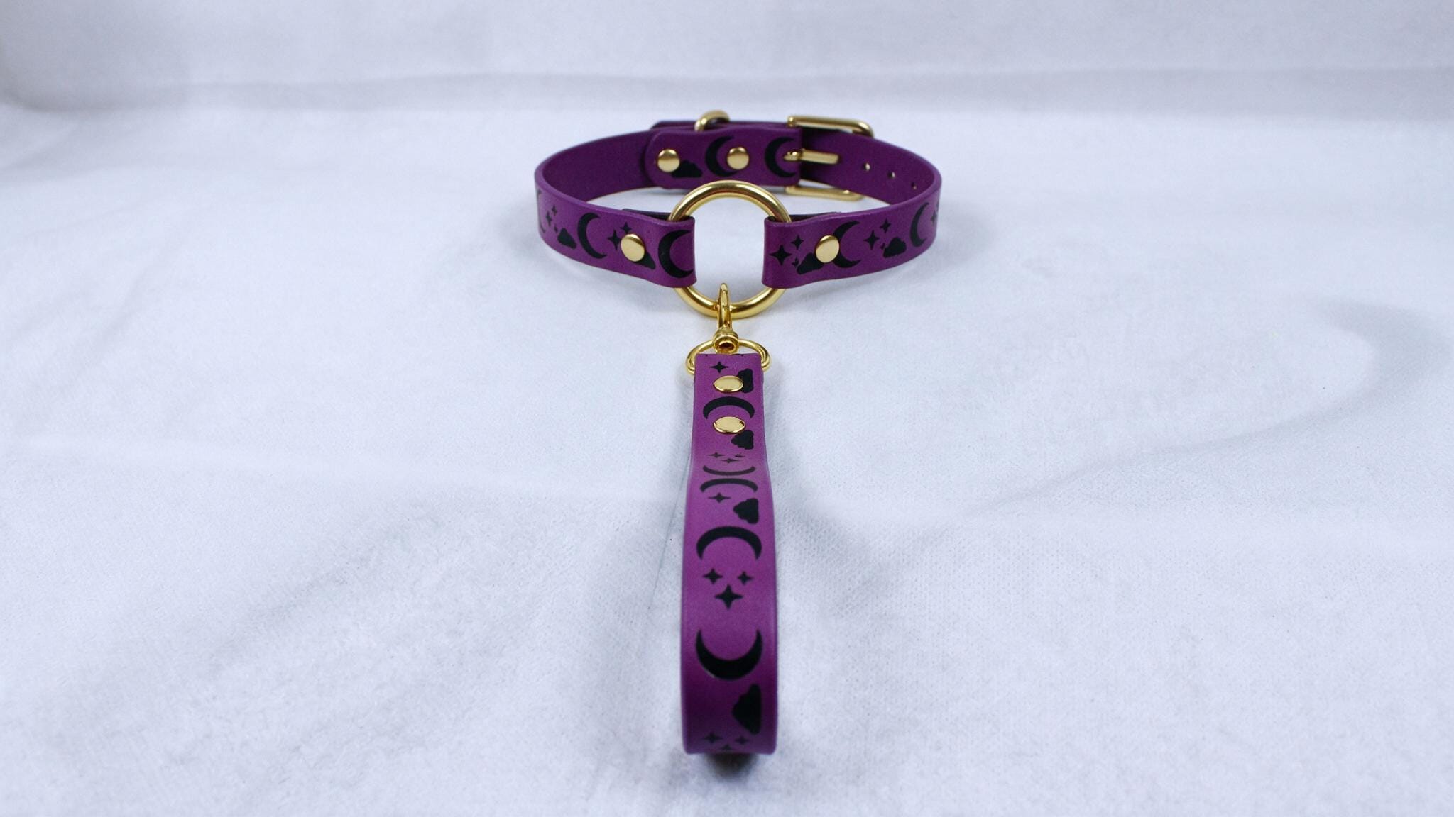 A purple collar with a gold buckle and a black star design is displayed on a white surface.
