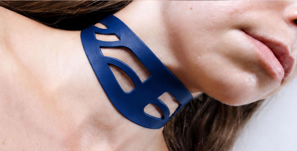 A close-up view of a woman's neck and chin wearing a blue, abstract-shaped necklace.