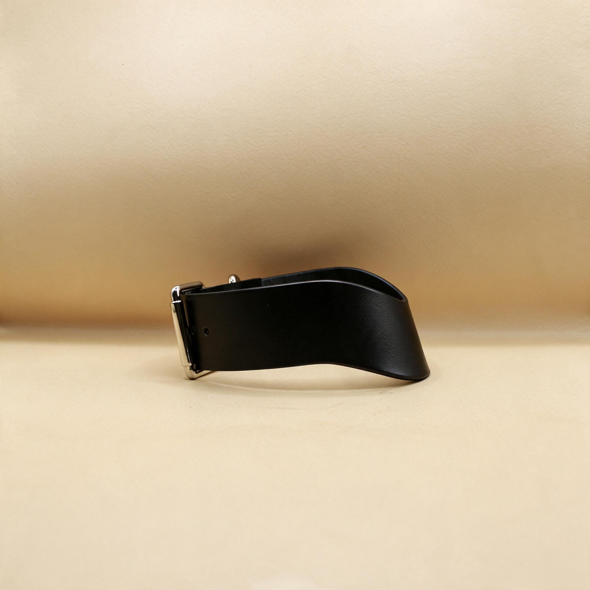 A black leather belt with a silver buckle is shown against a beige background.