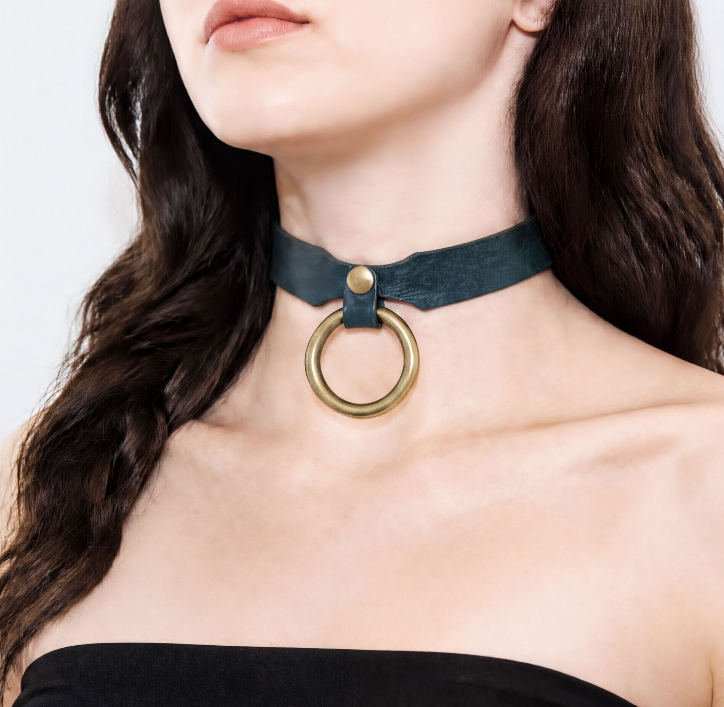 A close-up of a woman's neck and chest area wearing a green choker necklace with a gold ring.