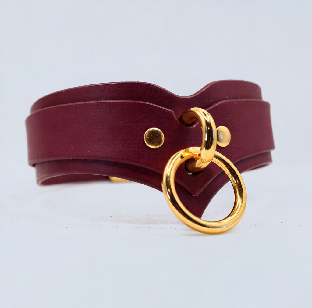 A burgundy leather choker necklace with a gold-colored metal ring and two gold-colored metal studs on the collar.