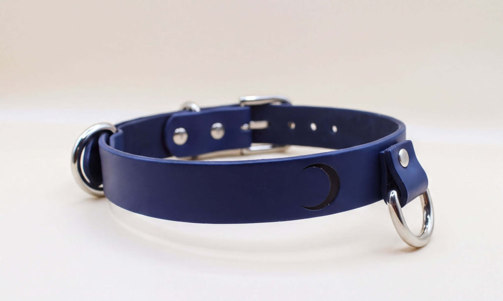A navy blue leather collar with silver metal rings and a crescent moon symbol on the front.