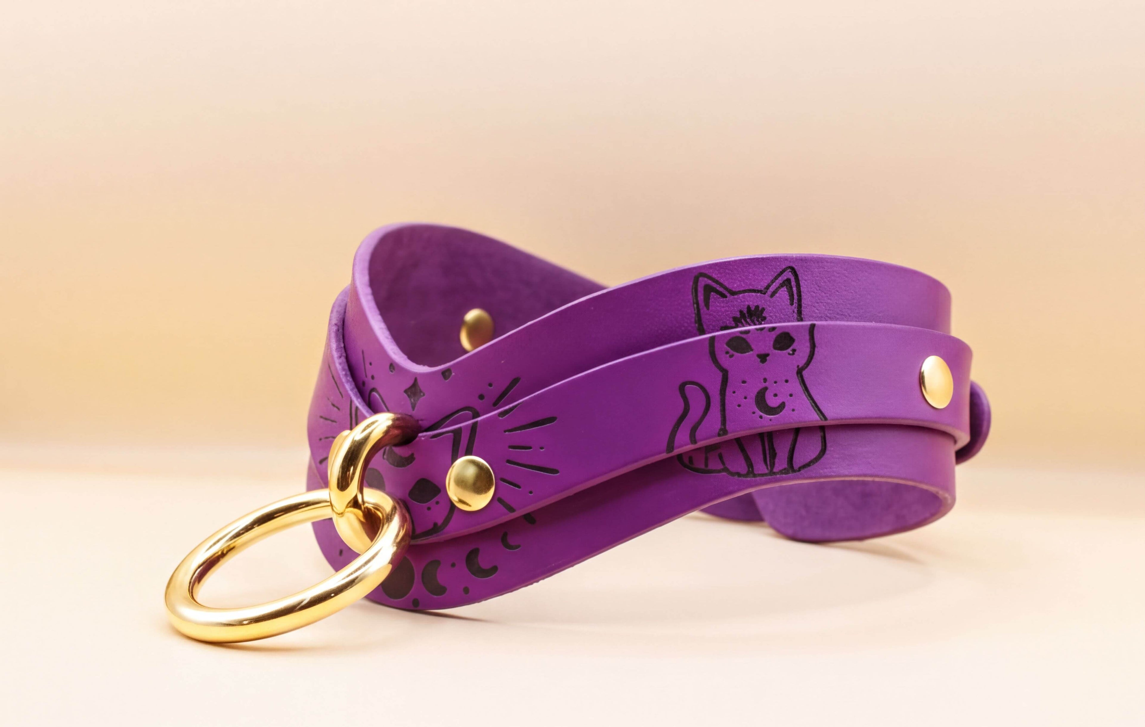 A purple leather choker necklace with a cat design and a gold ring.