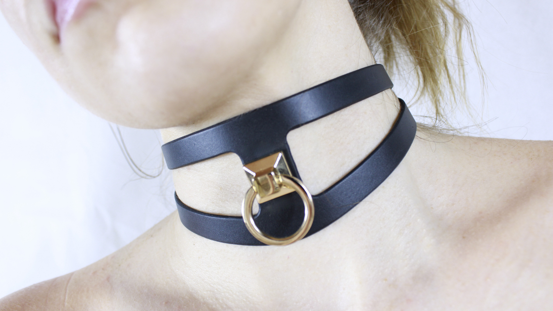 A close-up of a person's neck wearing a black choker necklace with a gold-colored metal ring.
