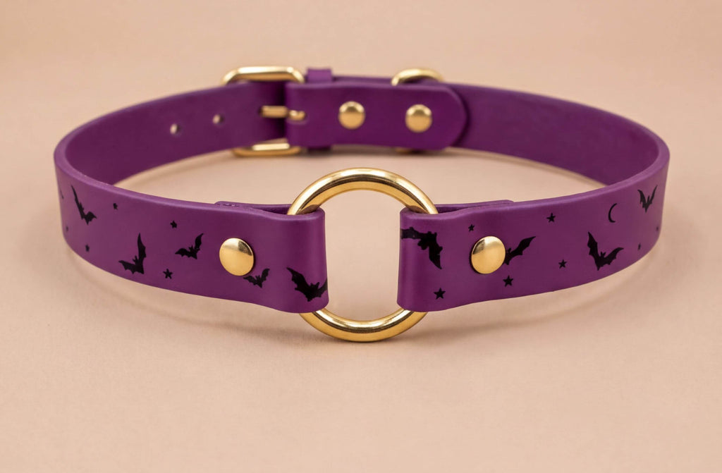 A purple leather collar with a gold ring and bat designs, featuring a purple band with black bats and stars.