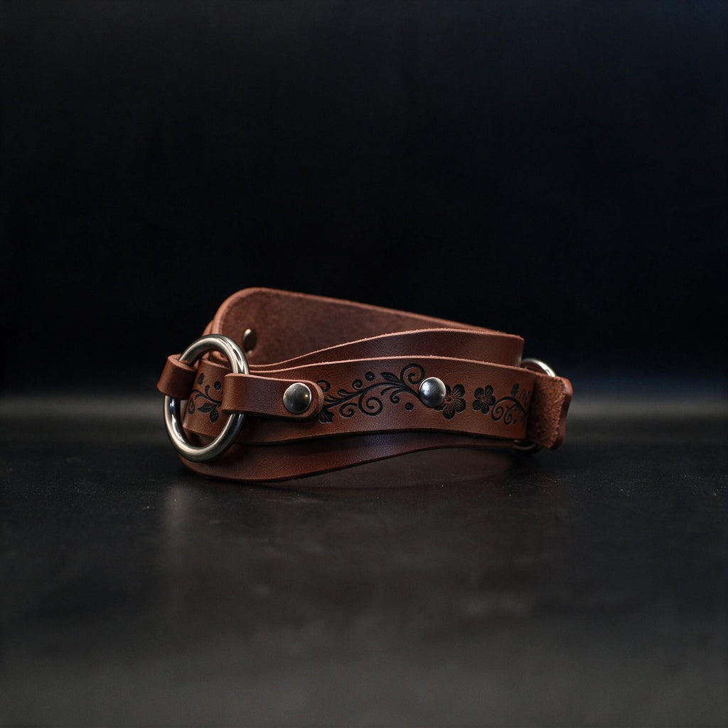 A brown leather belt with a metal buckle and decorative floral pattern on the strap is shown against a dark background.