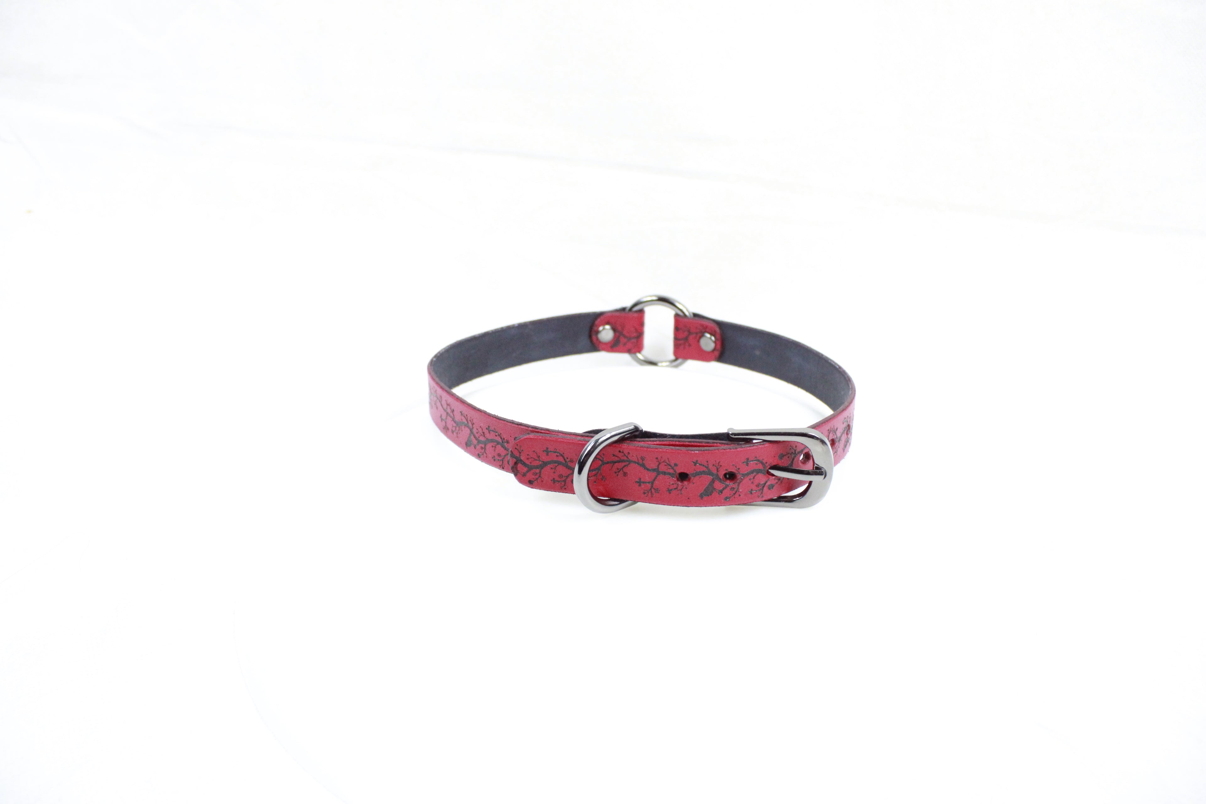 A red leather collar with a metal buckle and a floral pattern on the strap.