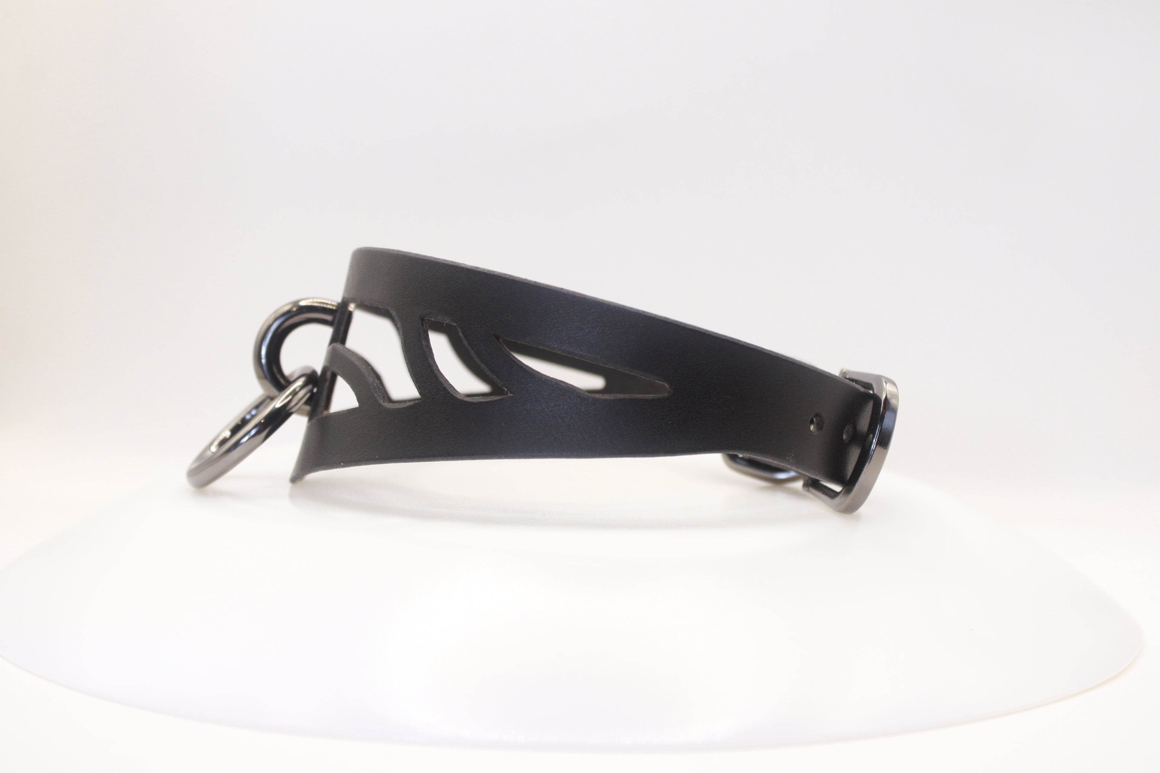 A black leather choker necklace with a cutout design and metal rings.