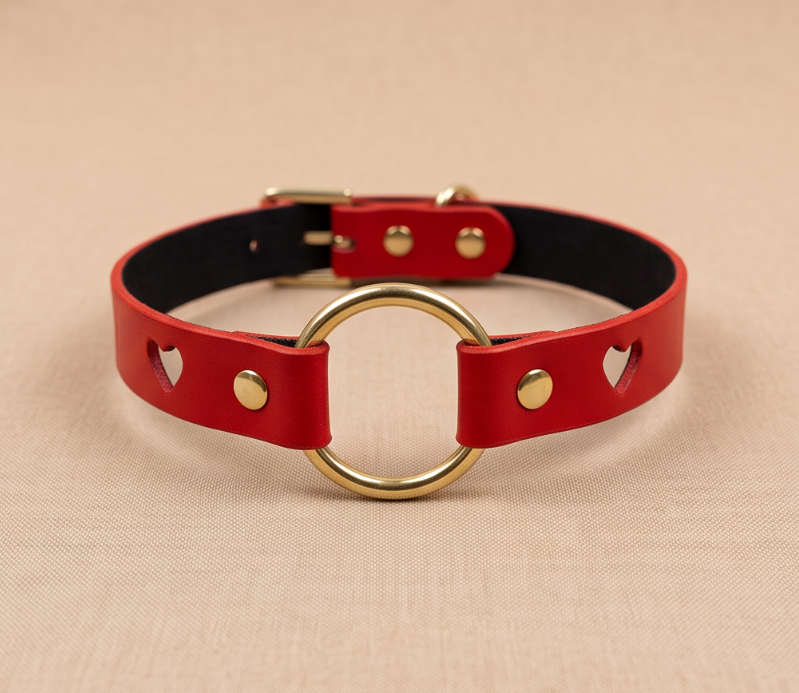 A red leather collar with a gold ring and heart-shaped cutouts on the sides.