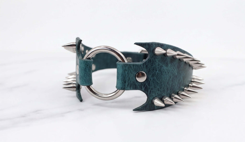 A green leather strap with silver spikes protruding from it, resting on a white marble surface.