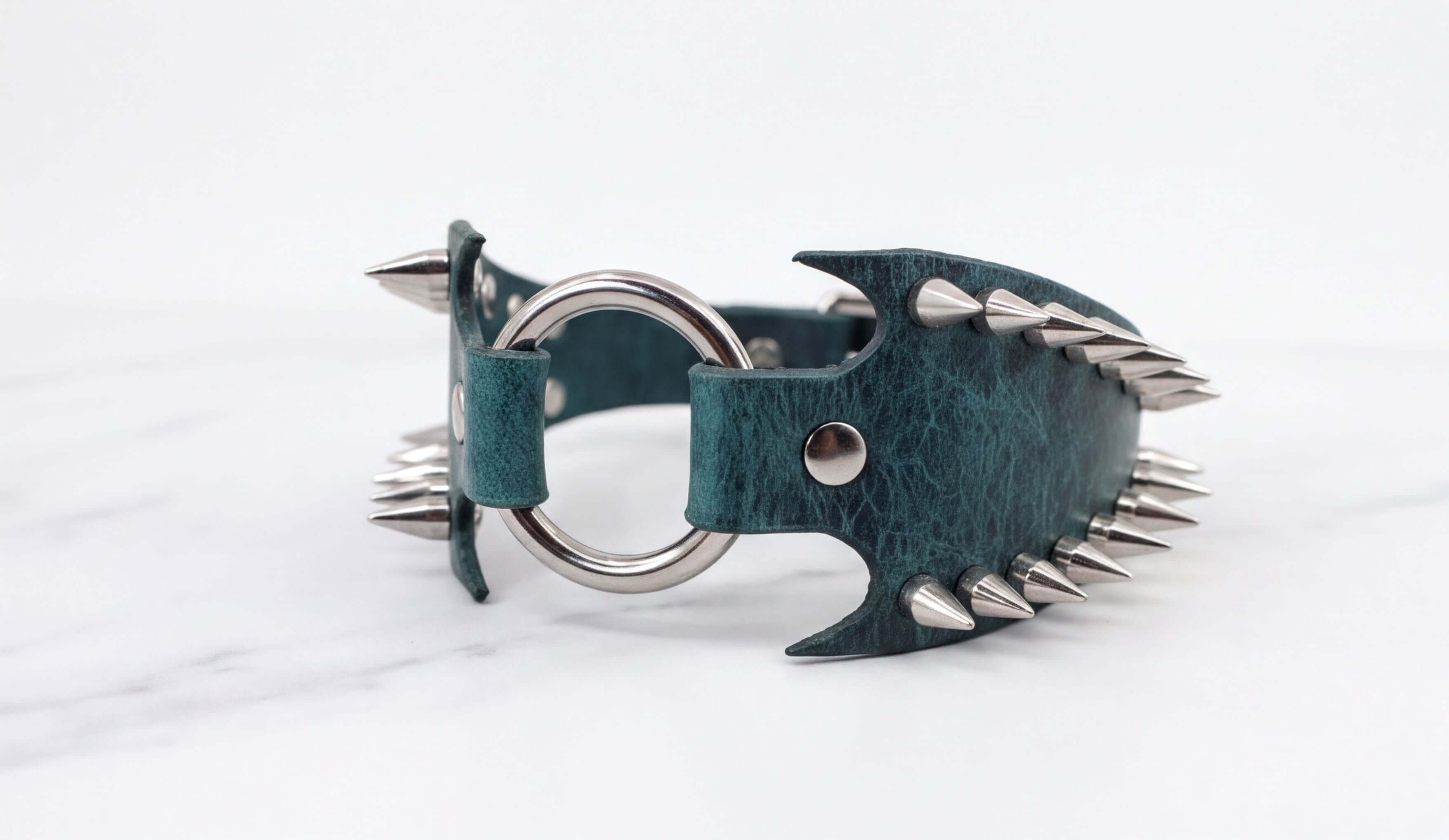 A green leather strap with silver spikes protruding from it, resting on a white marble surface.