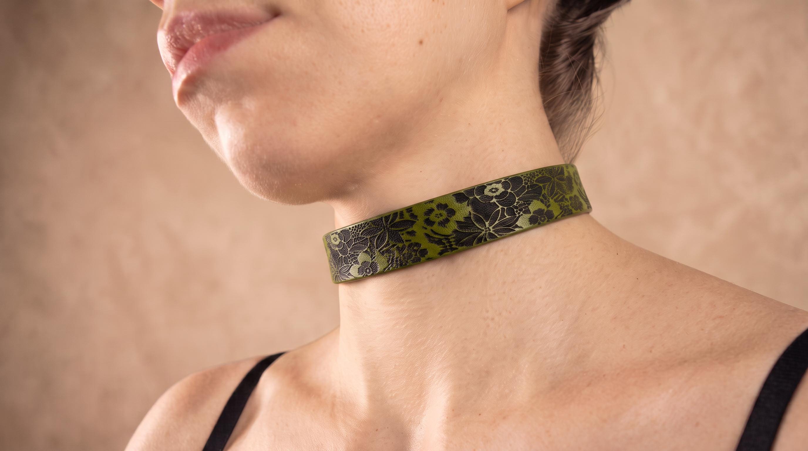 A close-up of a woman's neck and chest area wearing a green choker necklace with a floral pattern.