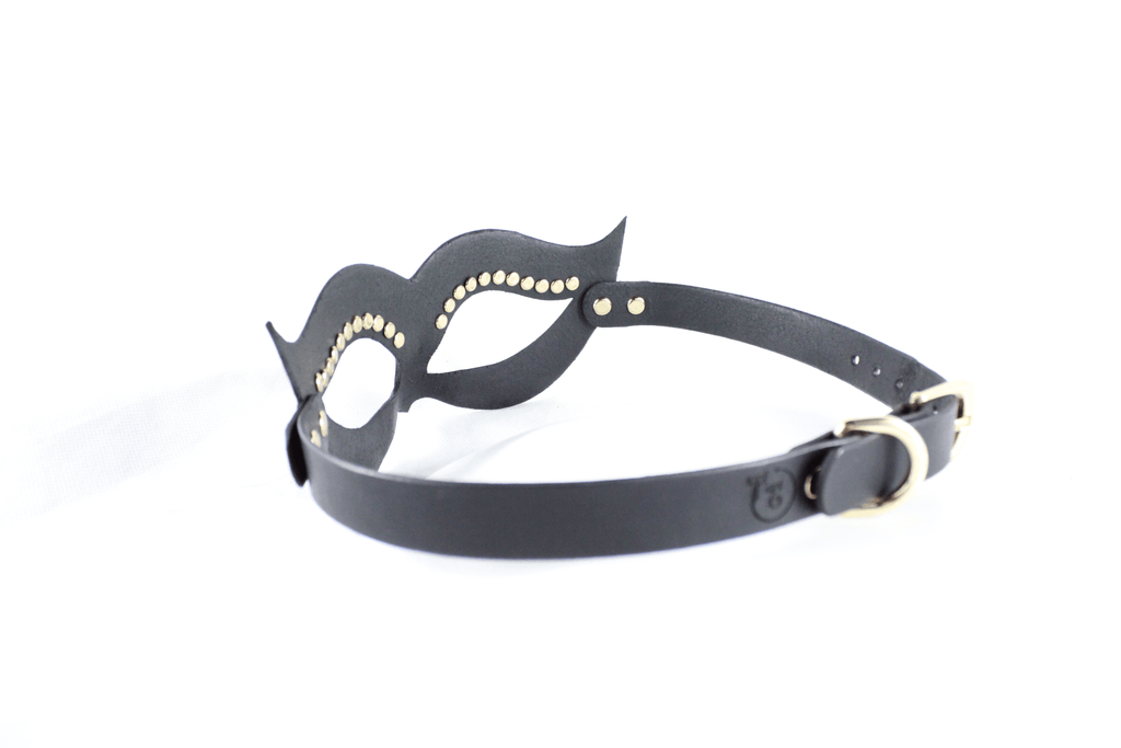 A black leather mask with gold studs on the sides and a black strap with a gold buckle.