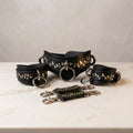 a collection of black leather straps with gold leaf designs, arranged on a white marble surface.