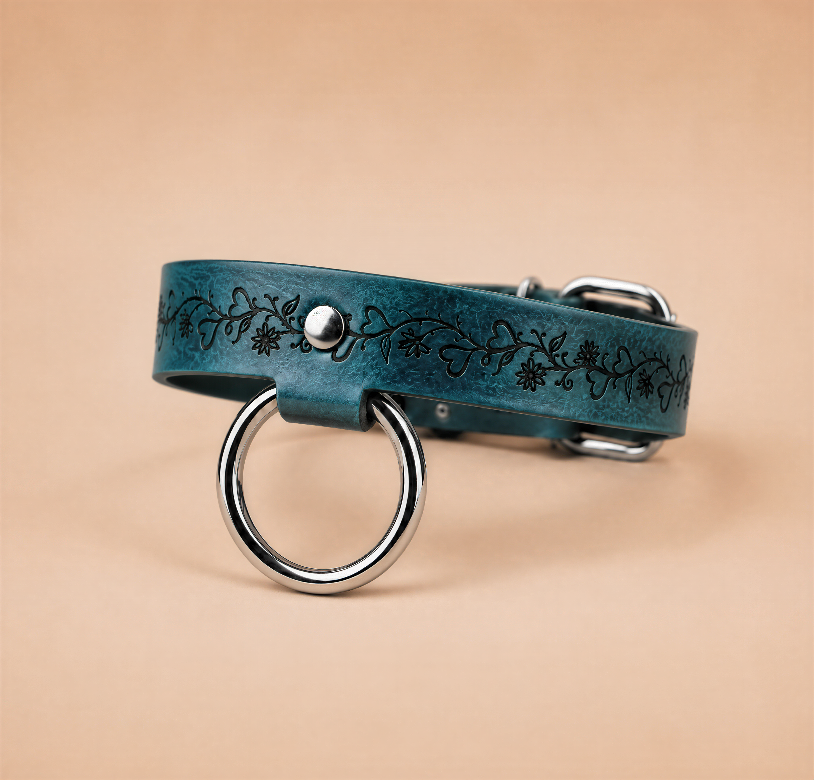 A blue leather collar with a metal ring and a floral design on it.