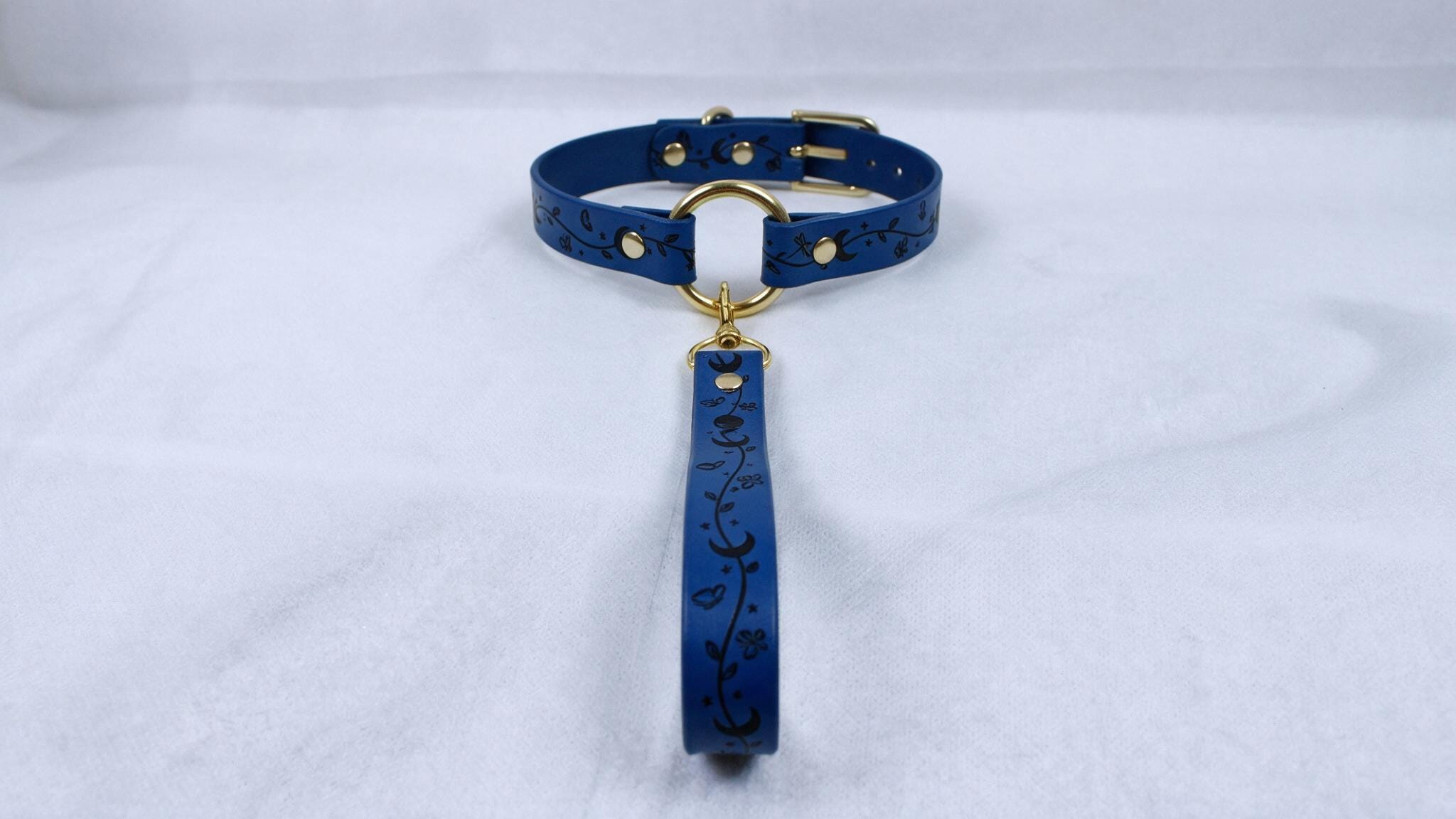 A blue collar with a gold buckle and a black floral pattern on the strap.