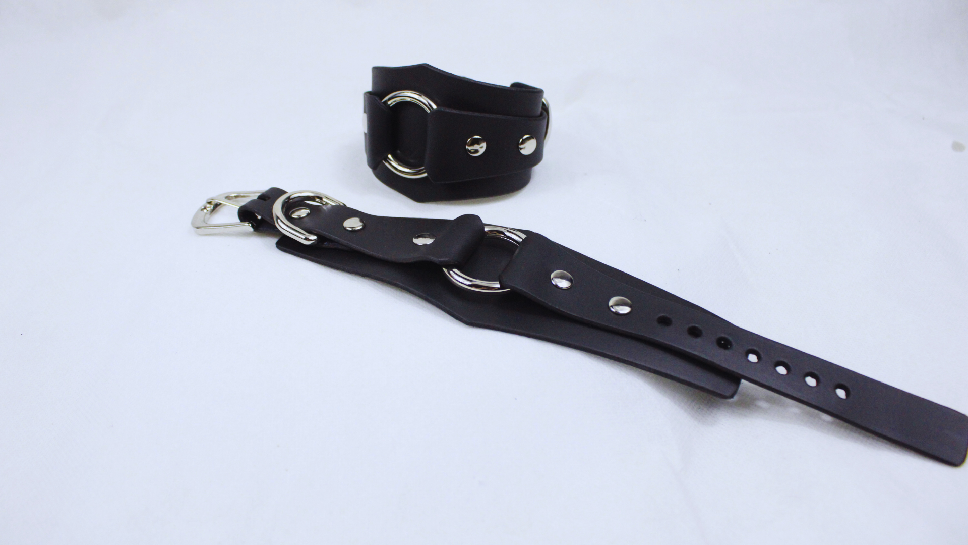 A black leather strap with metal buckles and holes is shown on a white background.