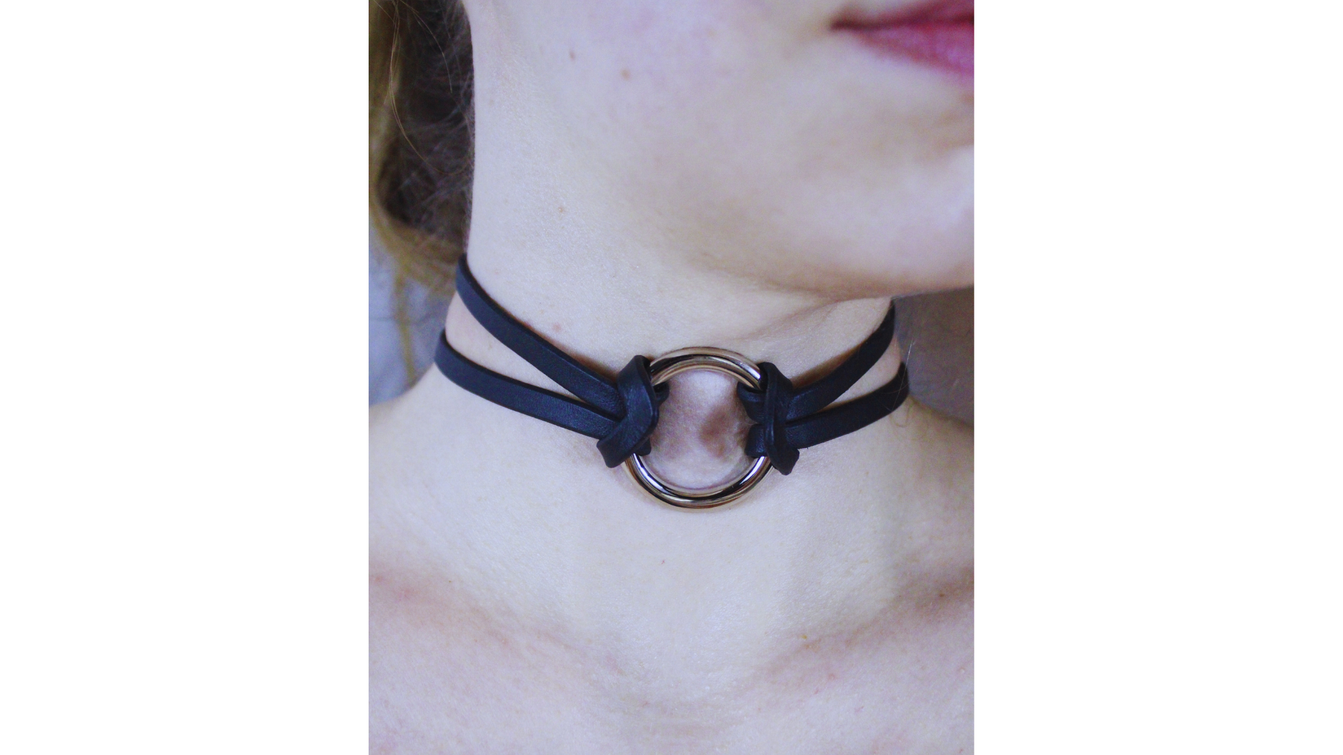A close-up view of a person's neck and chin area, featuring a black choker necklace with a circular metal ring.