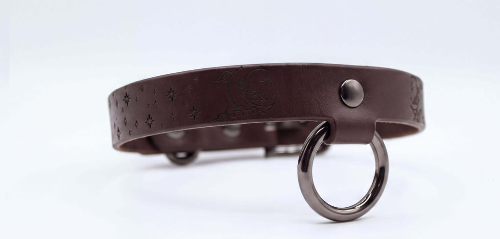 A brown leather collar with a metal ring and star-shaped designs on the surface.