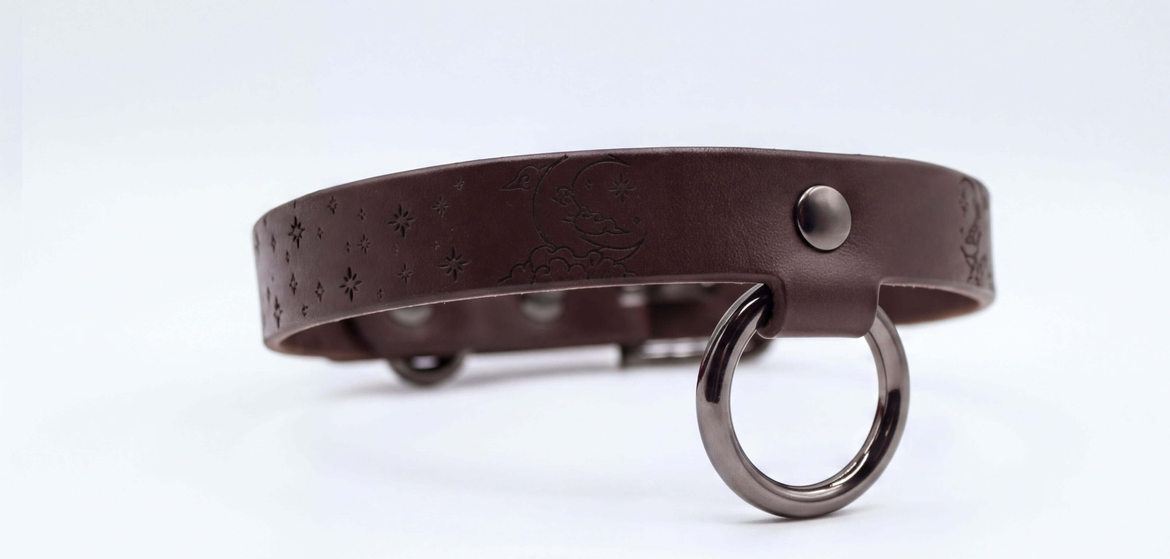 A brown leather collar with a metal ring and star-shaped designs on the surface.