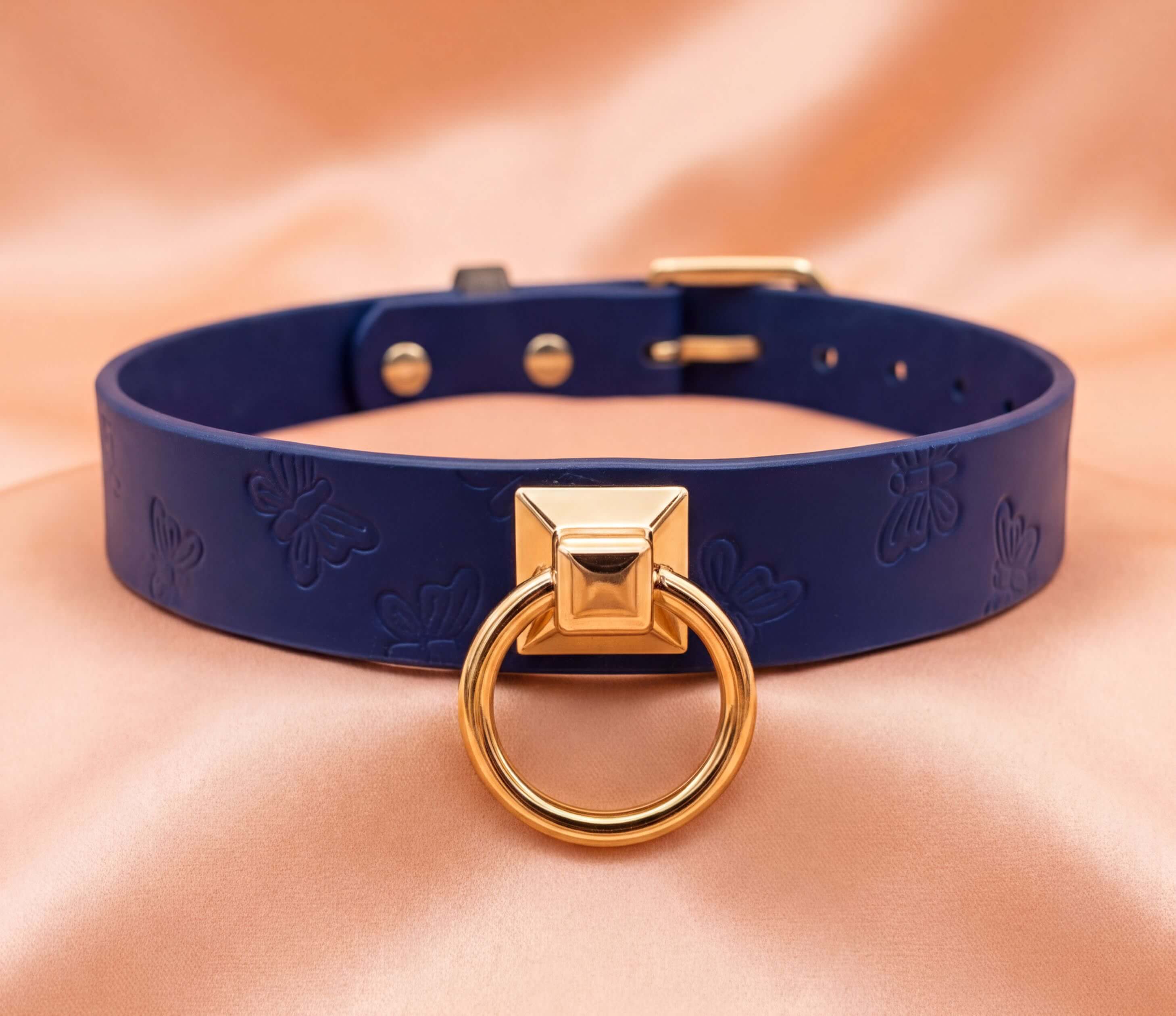 A blue leather choker necklace with a gold-colored metal ring and a small square metal piece on the front.