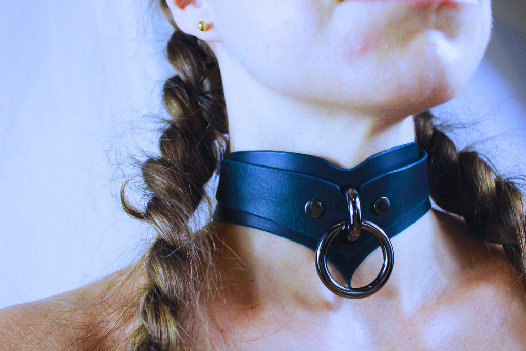 A close-up of a person's neck and chin wearing a blue leather choker necklace with a metal ring.