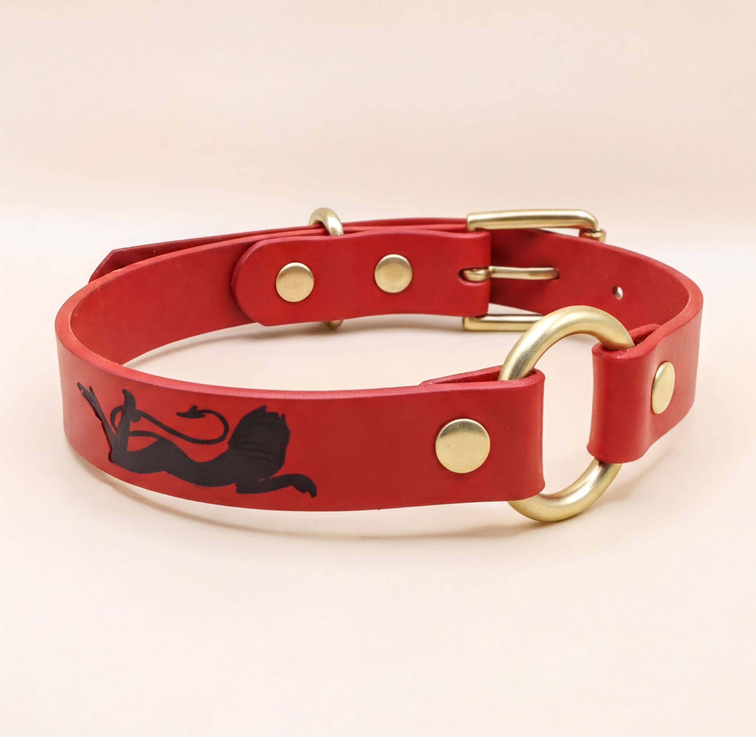 A red leather dog collar with a gold buckle and a black lion graphic on the front.