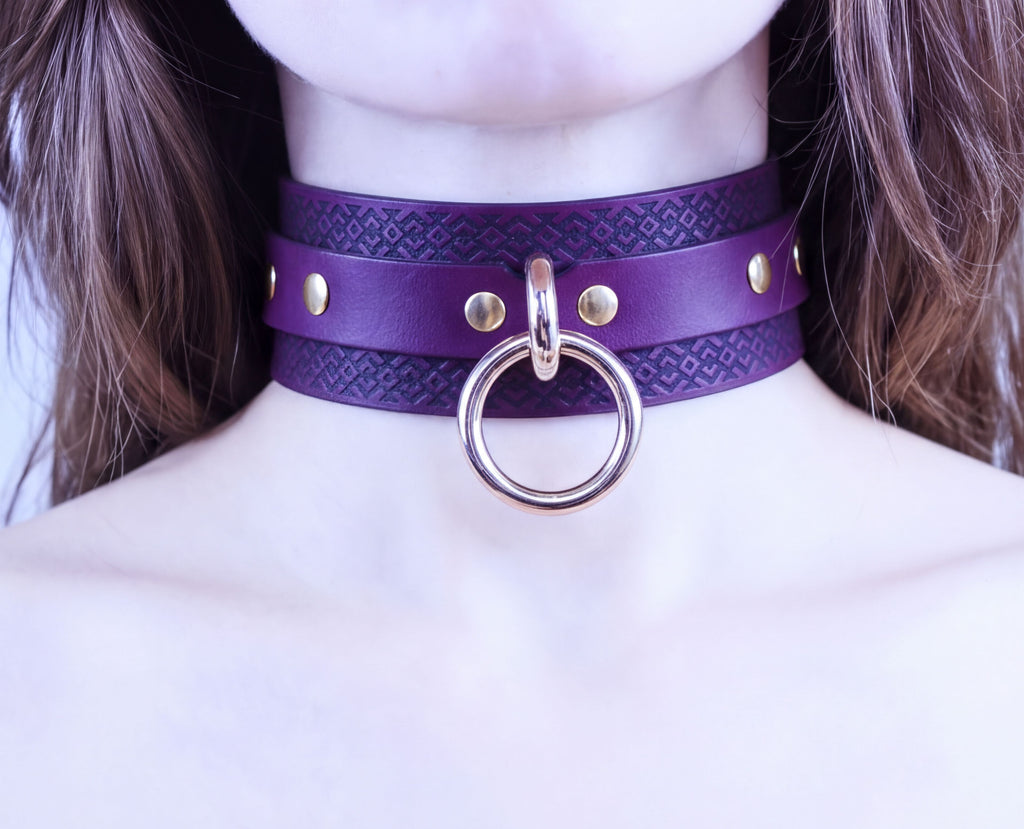 A close-up of a person's neck wearing a purple leather choker necklace with a gold ring and studs.