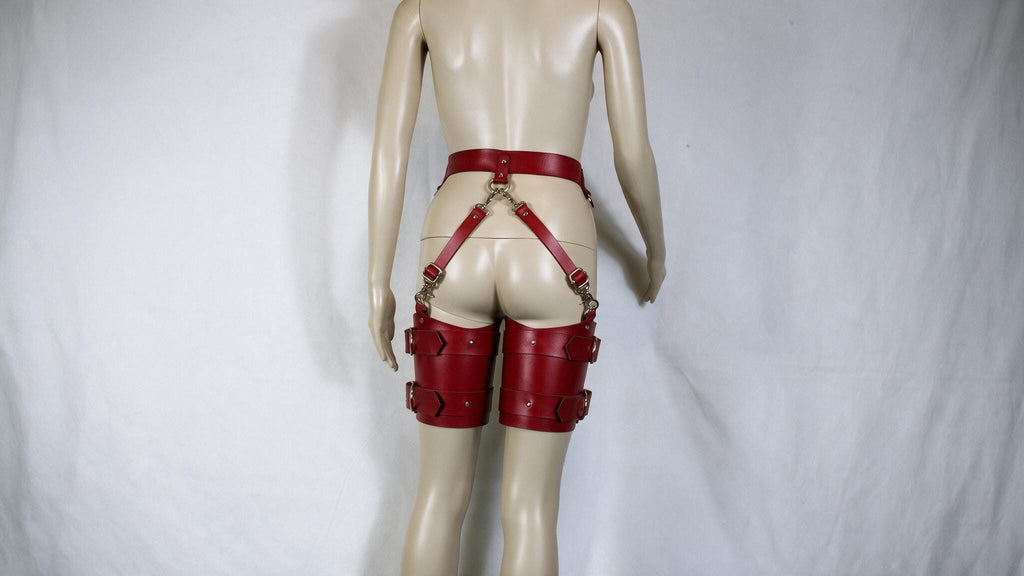 A mannequin wearing red leather garter belts and garter cuffs against a white background.