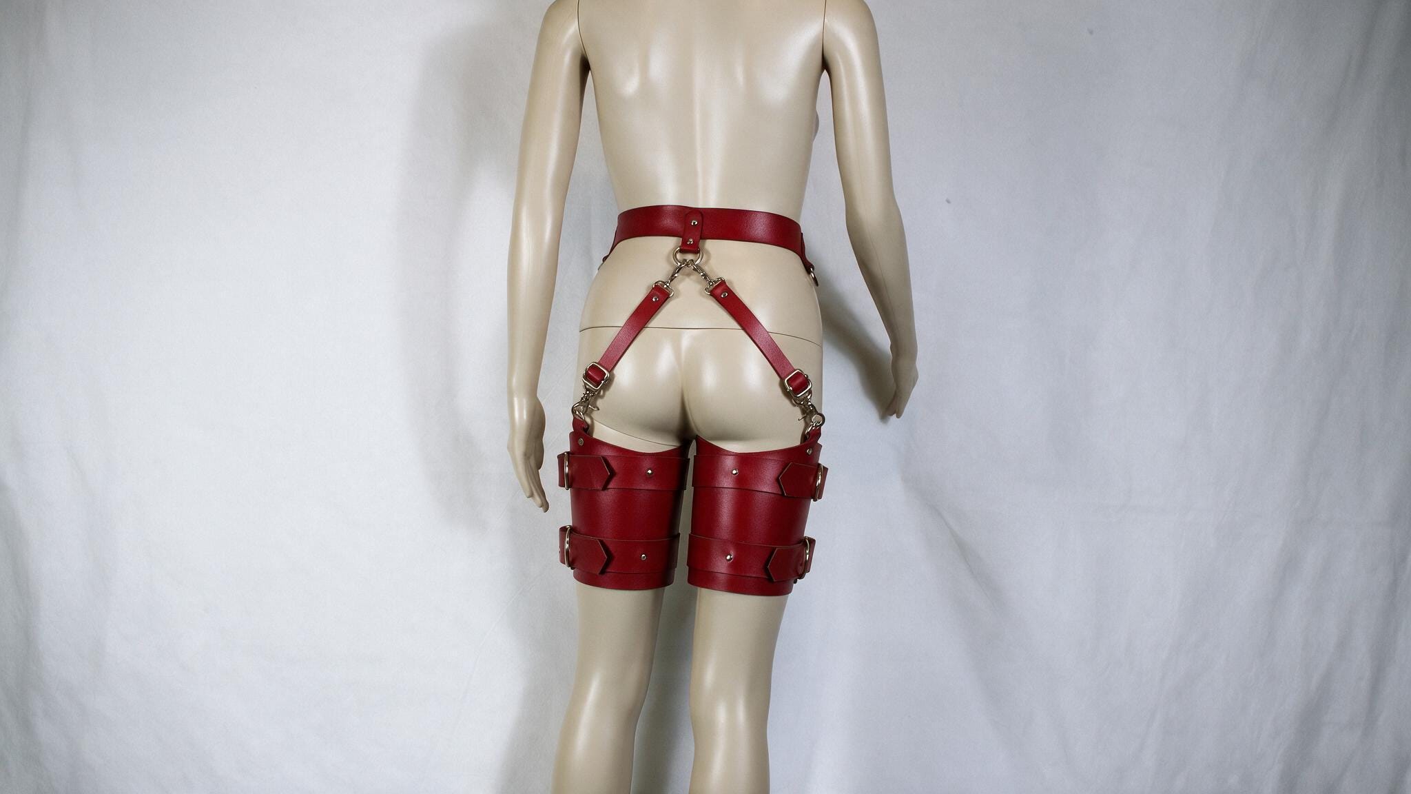 A mannequin wearing red leather garter belts and garter cuffs against a white background.