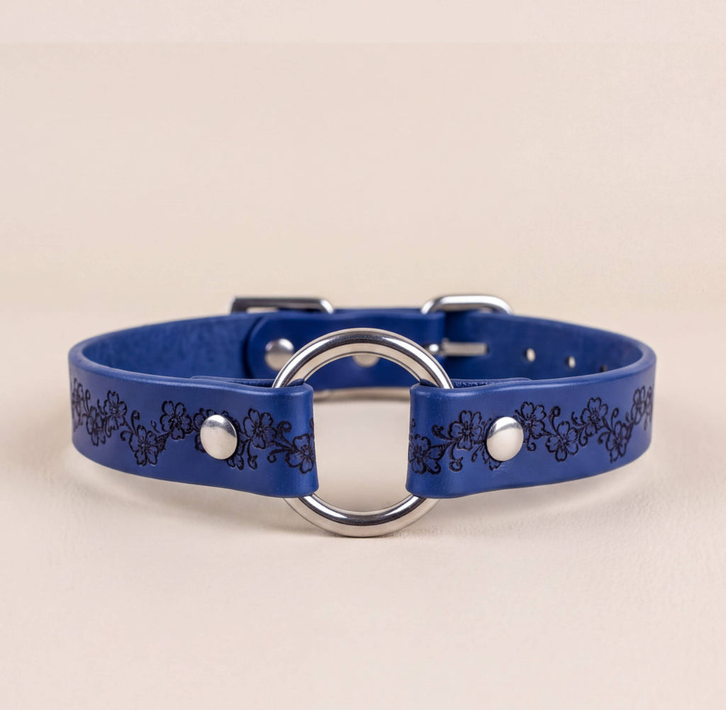 A blue leather collar with a silver metal ring and decorative floral pattern.