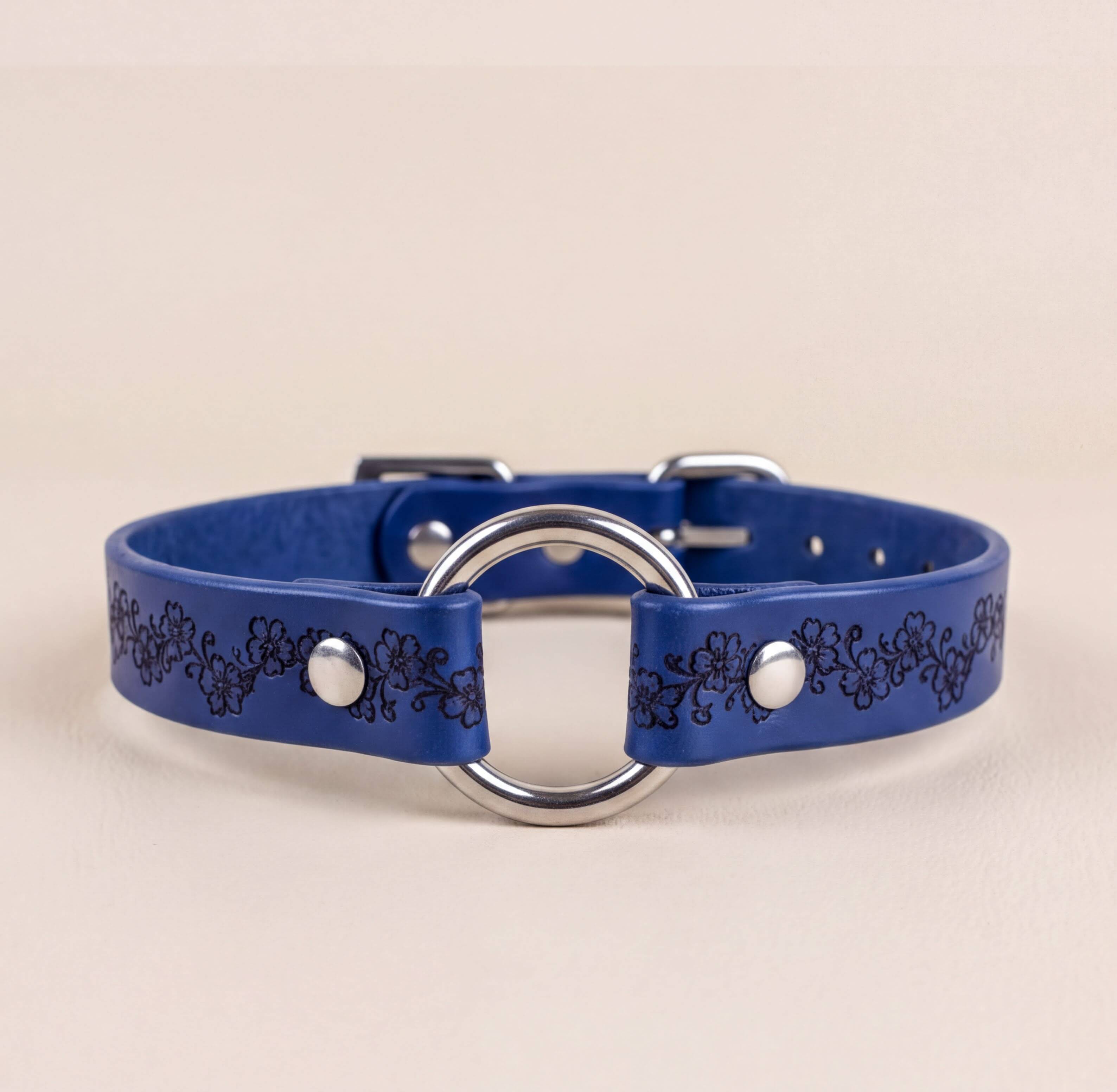 A blue leather collar with a silver metal ring and decorative floral pattern.