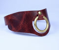 A close-up image of a red leather choker necklace with a gold-colored circular buckle.
