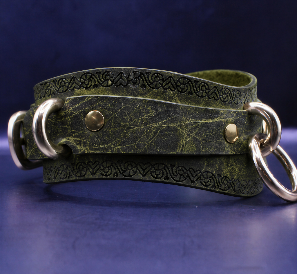 A green leather strap with metal rings and a decorative pattern on it, resting on a dark blue surface.