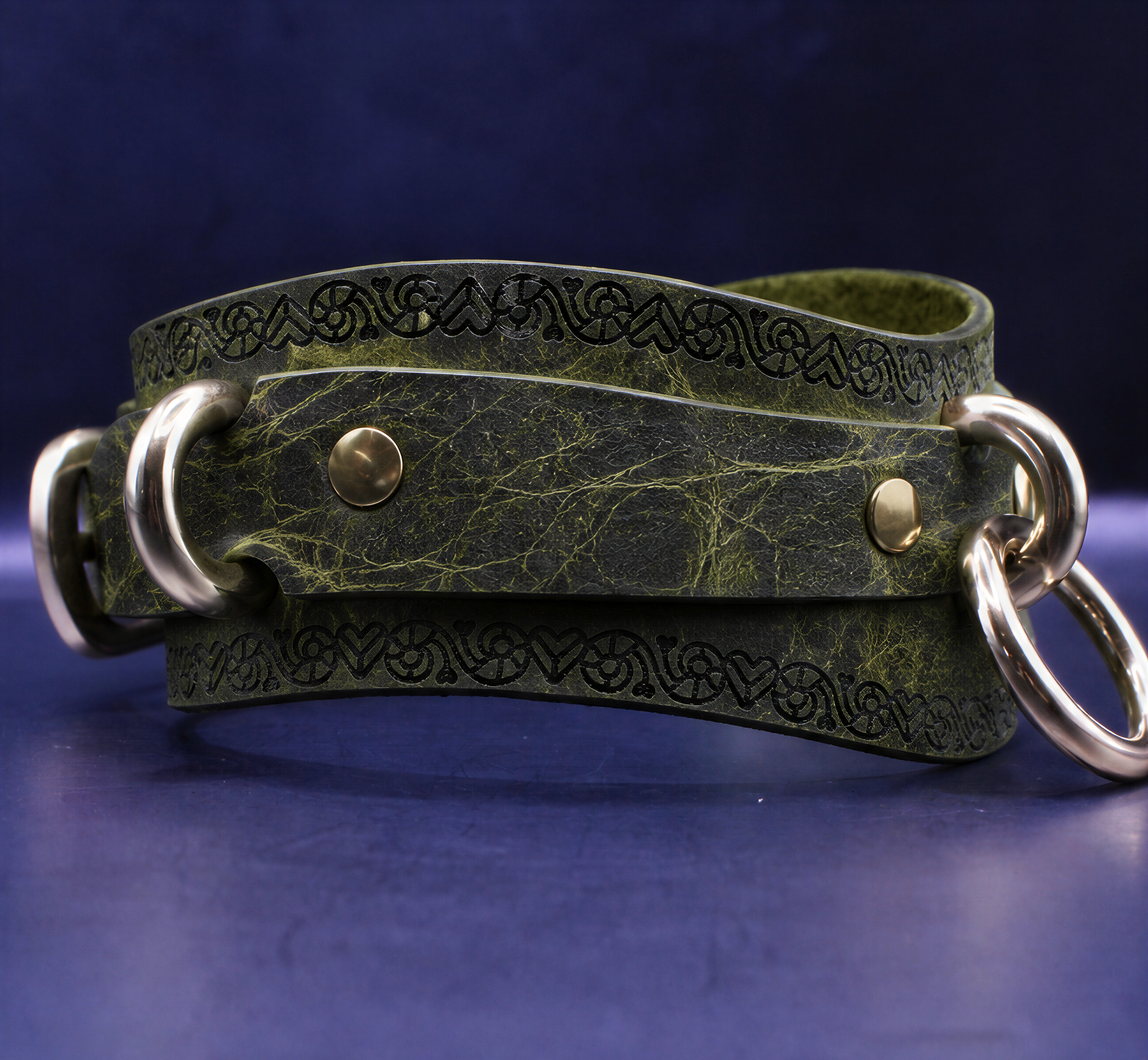 A green leather strap with metal rings and a decorative pattern on it, resting on a dark blue surface.