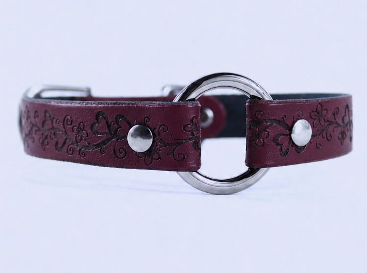 A burgundy leather collar with a circular metal buckle and floral designs.
