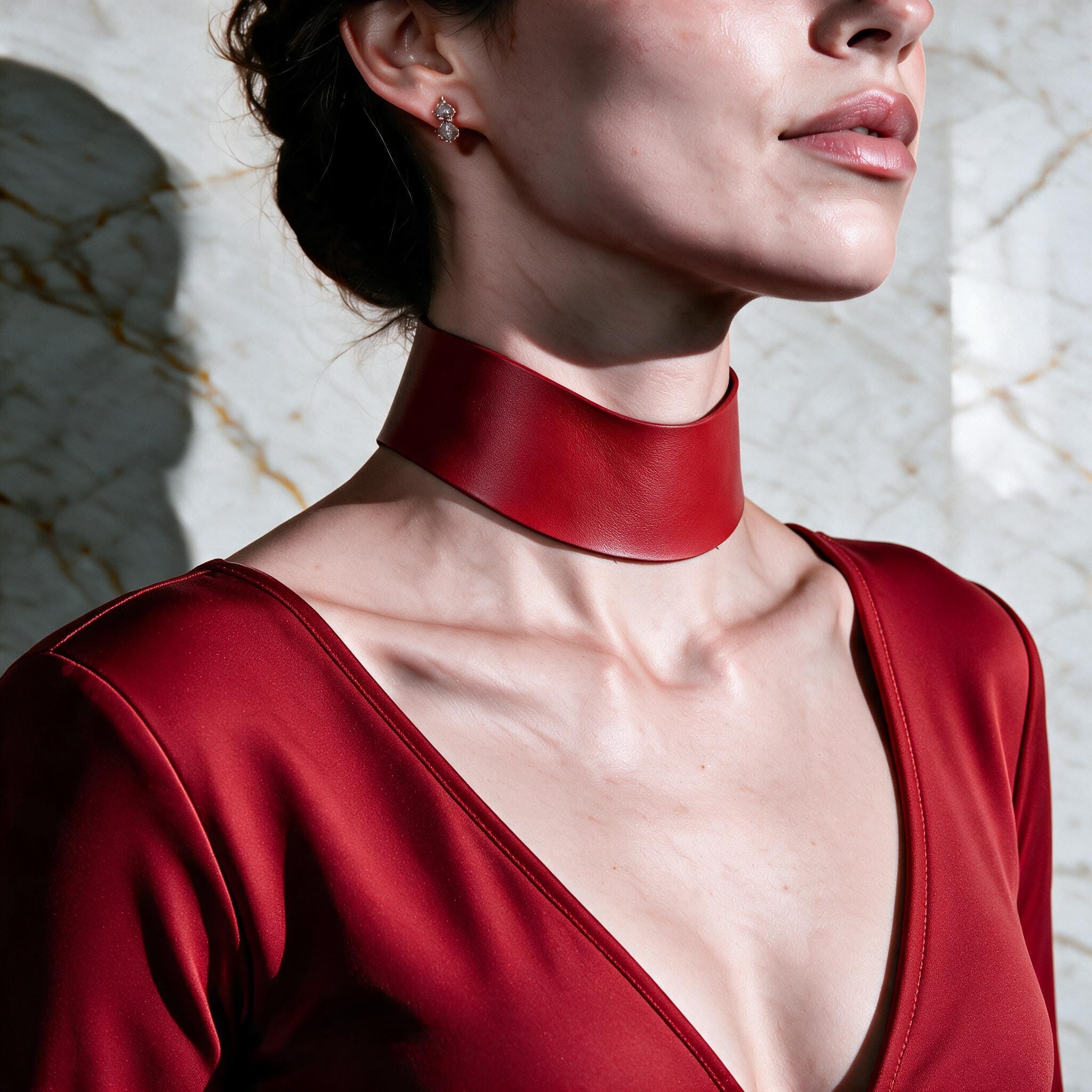 A woman wearing a red dress with a choker necklace stands against a marble wall.