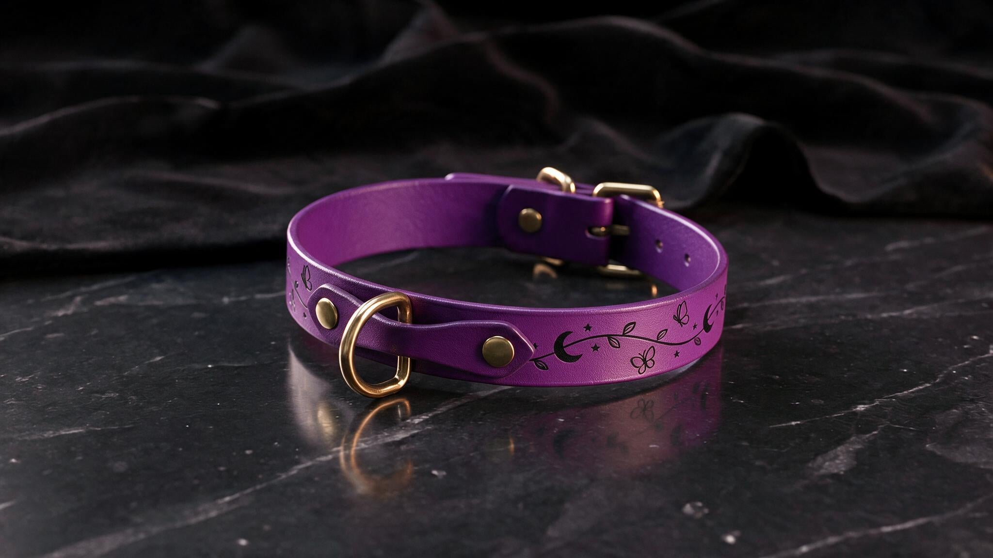 A purple leather collar with a floral design and gold hardware is displayed on a black marble surface.