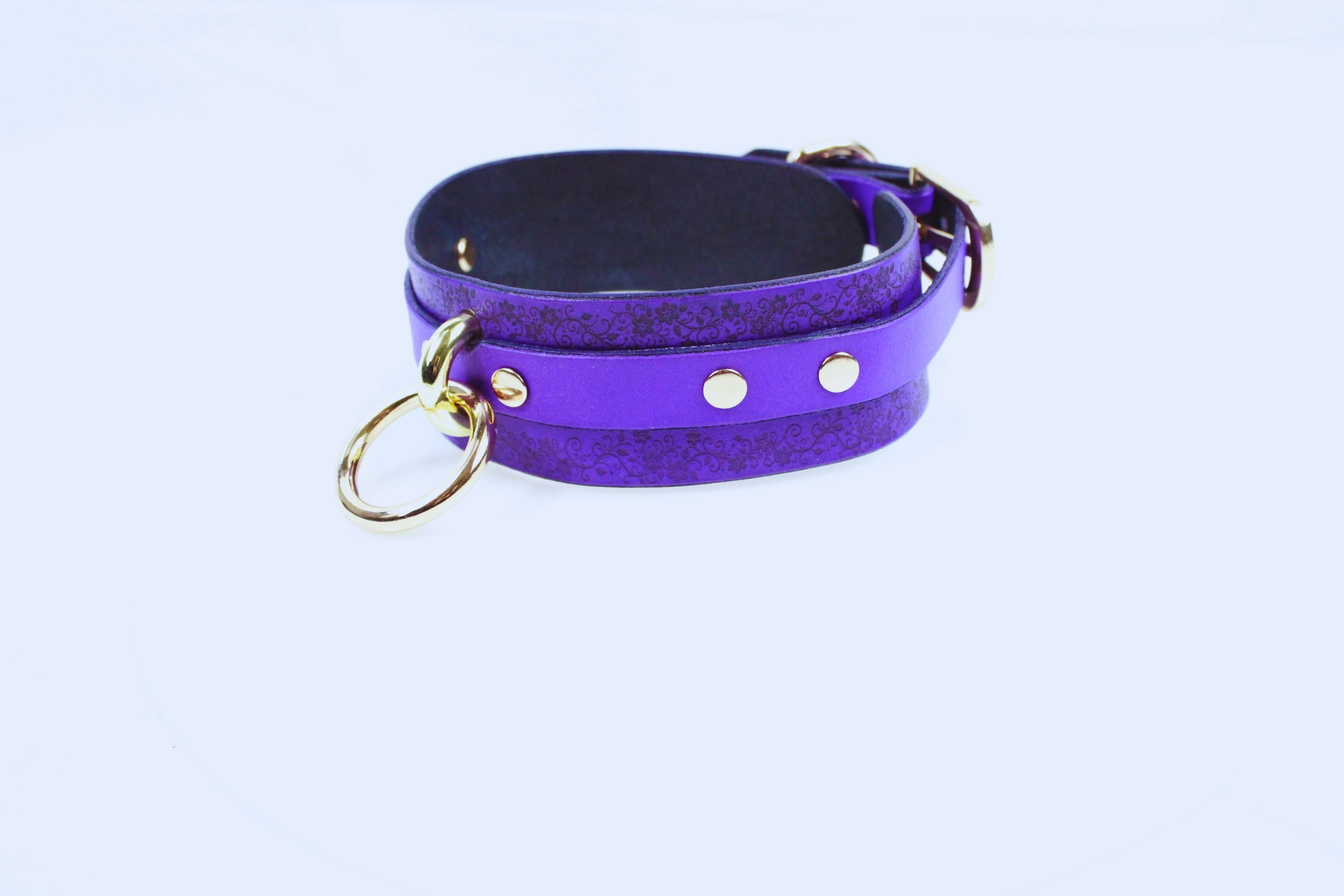 A purple leather choker necklace with a gold-colored metal ring and three small round buttons.