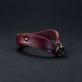 A burgundy leather choker necklace with a metal clasp and buckle is shown against a dark background.
