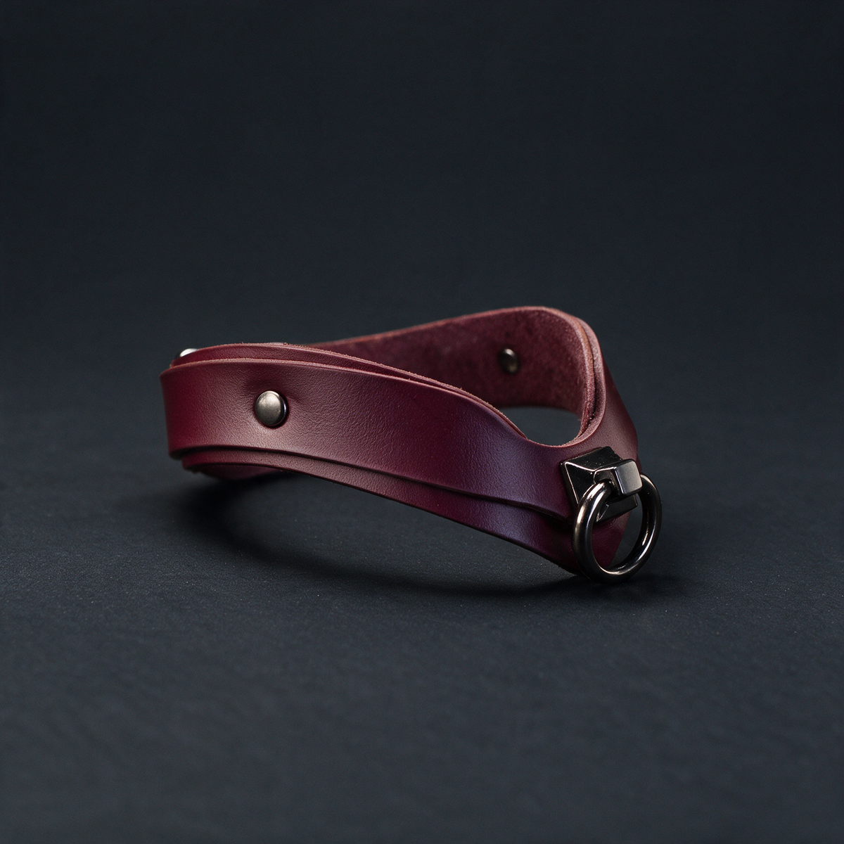 A burgundy leather choker necklace with a metal clasp and buckle is shown against a dark background.