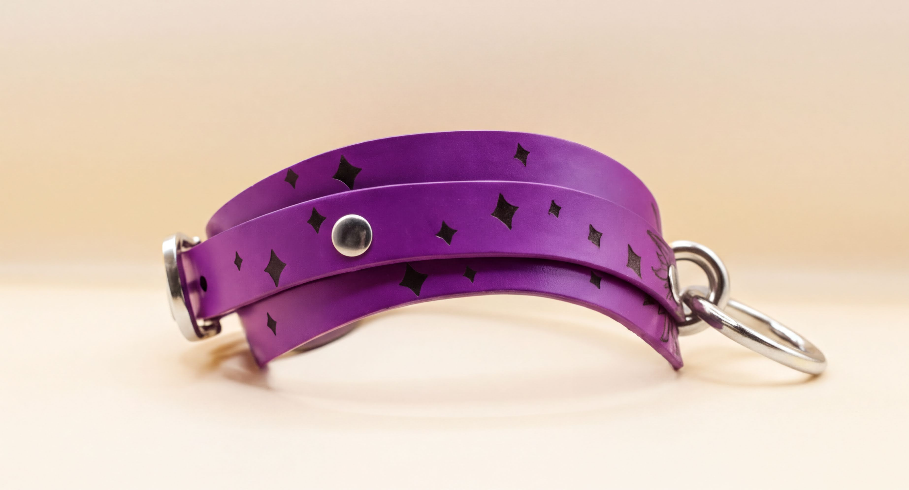 A purple leather strap with black diamond-shaped patterns and metal rings attached to it.