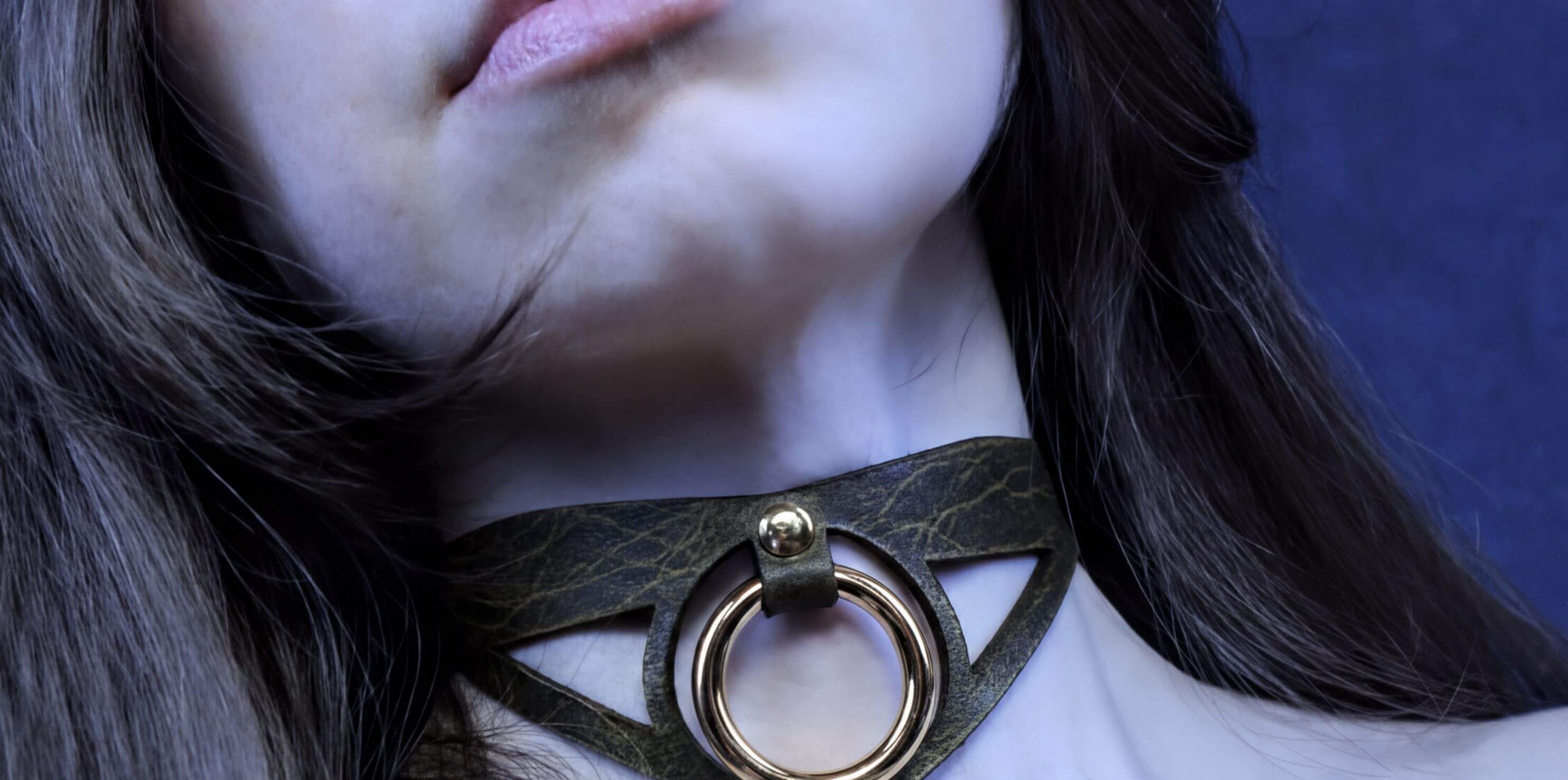 A close-up of a woman's neck and chin area, featuring a choker necklace with a circular metal ring.