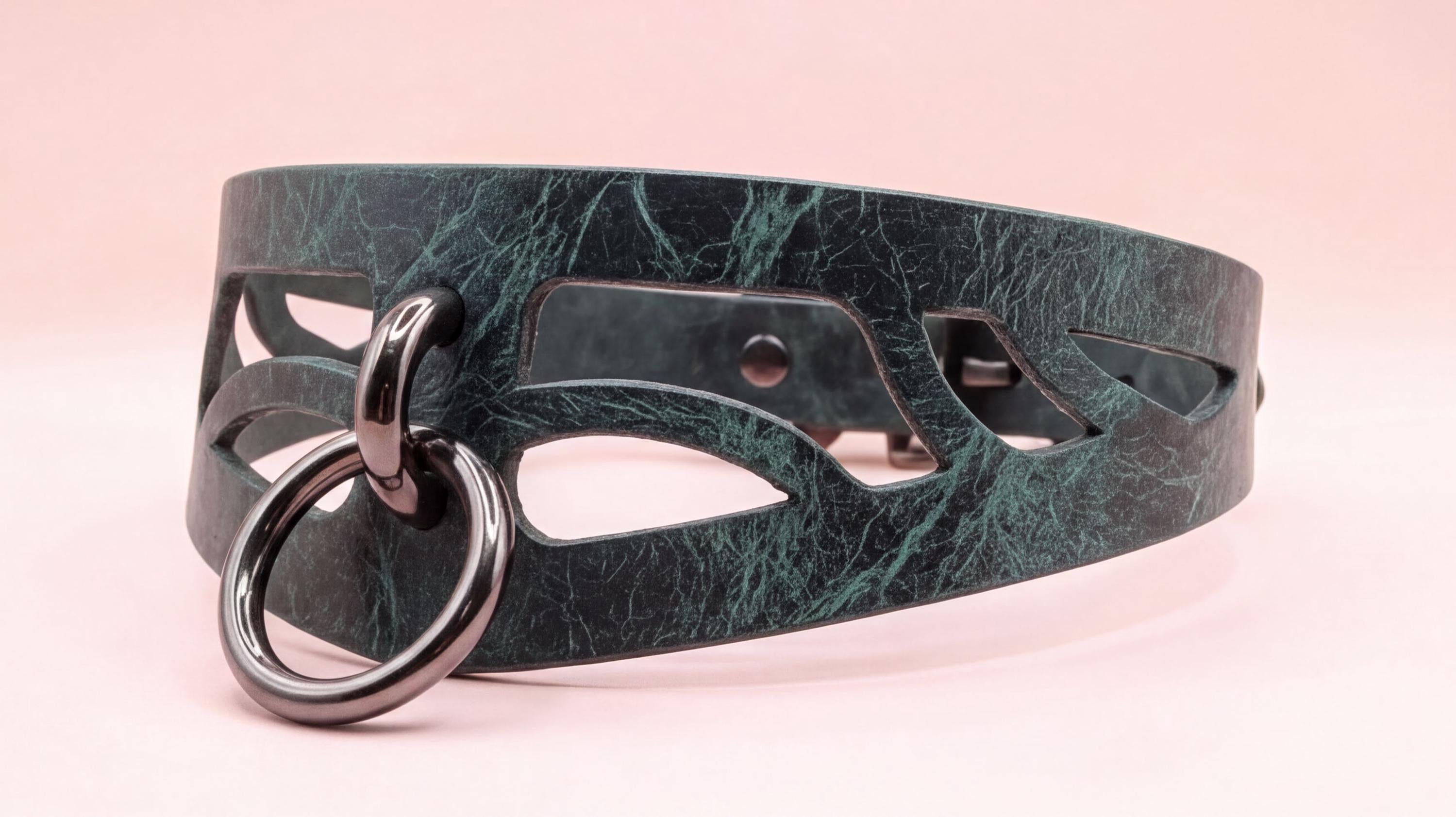 A close-up view of a dark green leather choker necklace with a metal ring and cutout design.